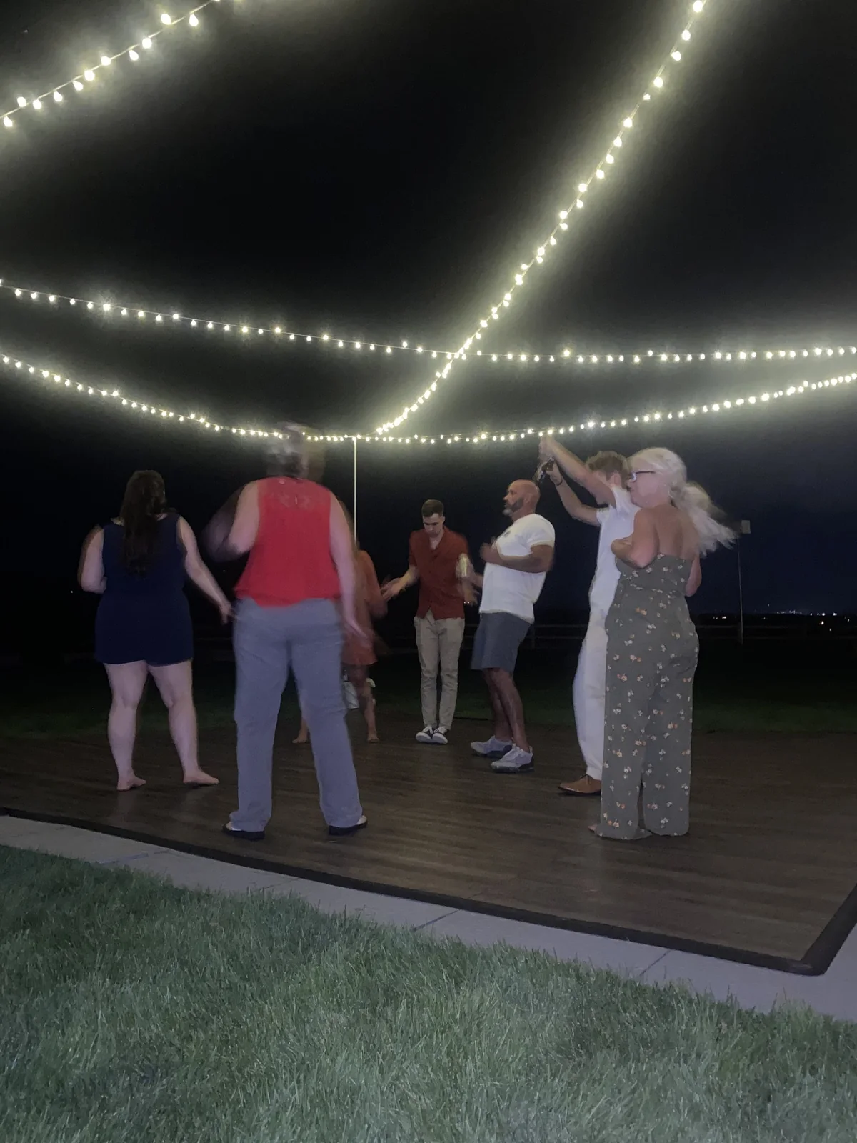 Guests dancing beneath string lights at an outdoor wedding